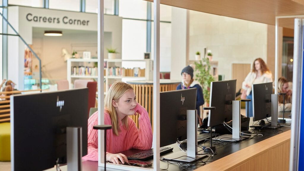 A student using computers on the first floor of Catalyst. Careers Corner can be seen in the background.