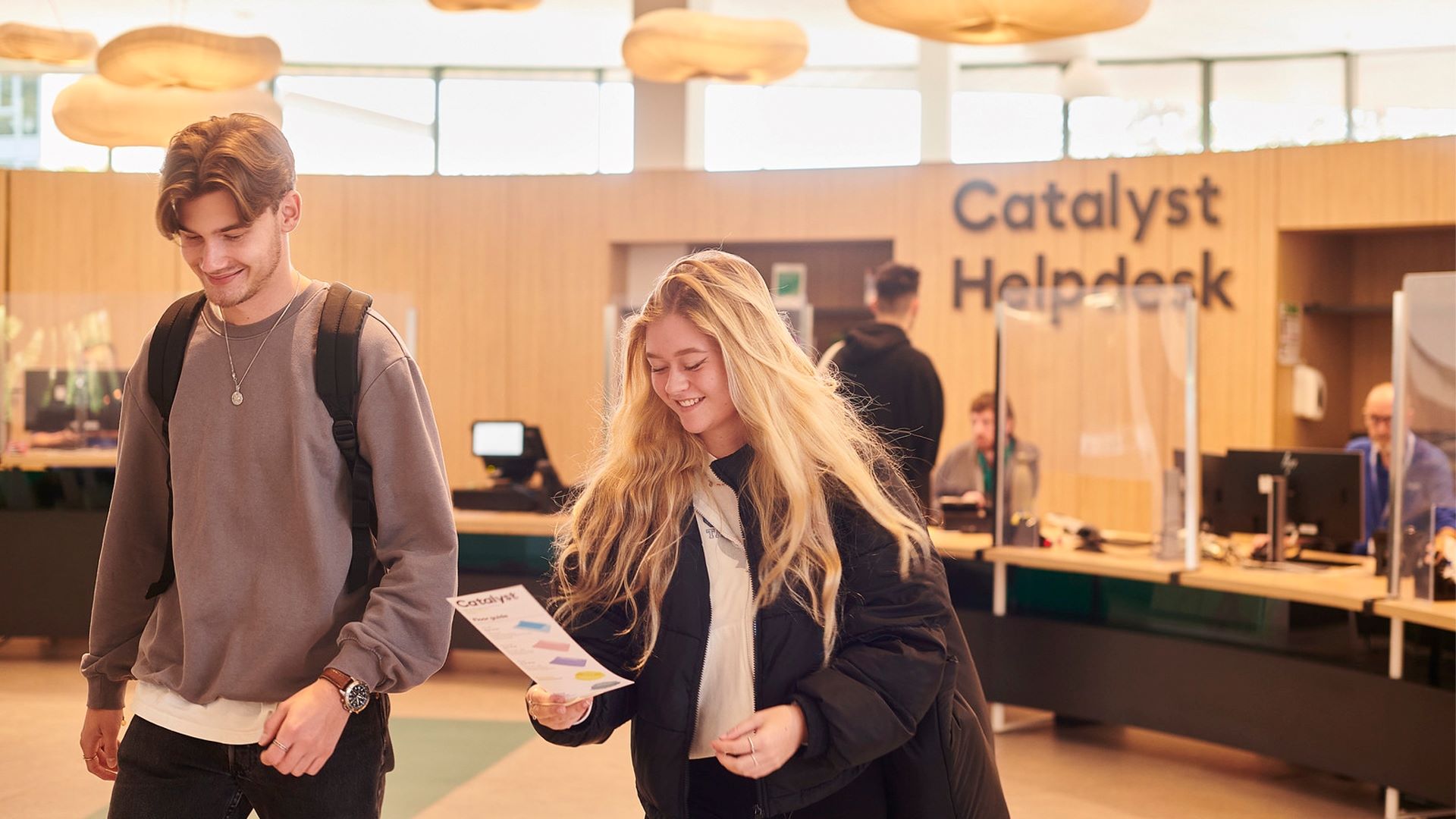 Two students walk from Catalyst helpdesk smiling and chatting.