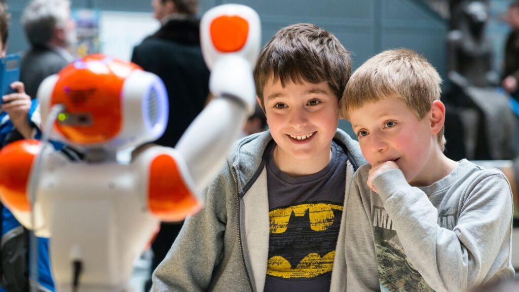 Two children with a red and white robot smiling.