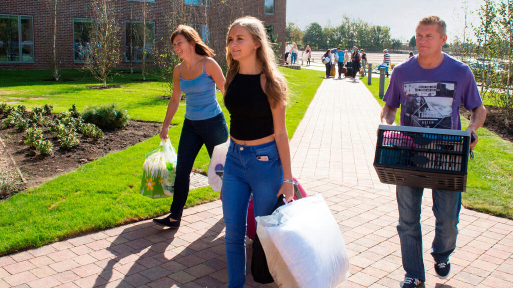 A student and their parents carry crates and bags as they prepares to move into their room on campus.