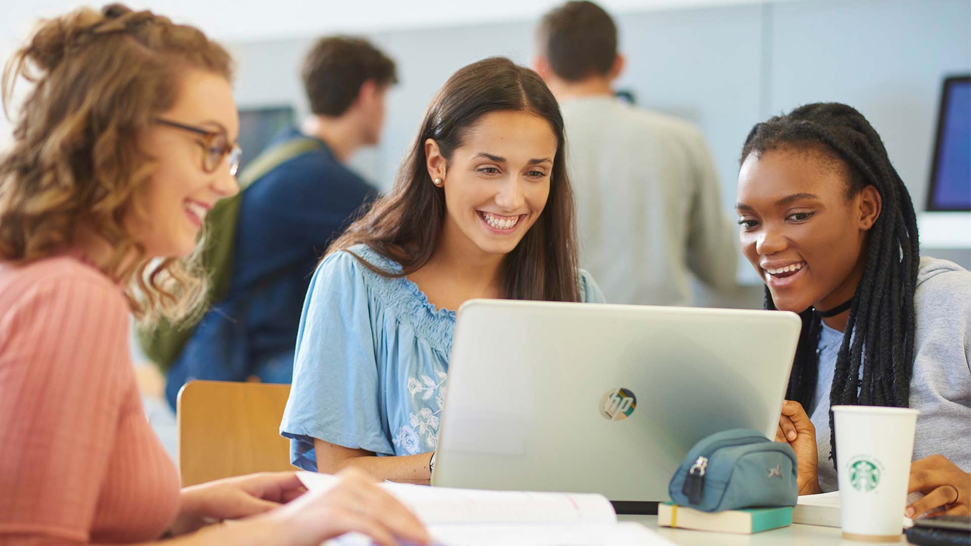 Three students smile as they look at something on a laptop