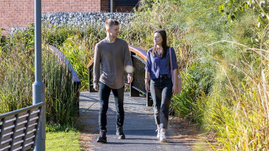 Two students walking across the bridge by lakeside