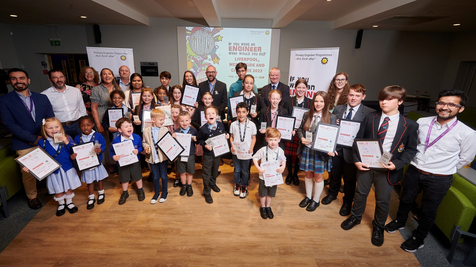 Large group of Primary staff and students stand holding certificates for their engineering ideas at Edge Hill University.