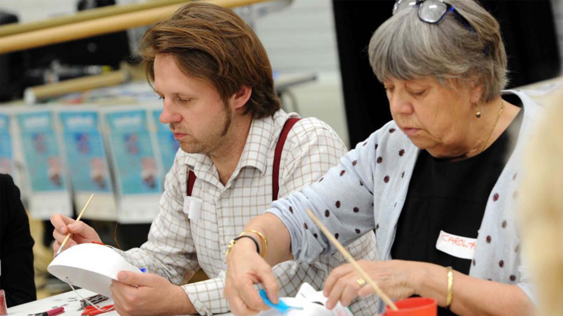 A man and a woman taking part in arts and crafts whilst sat at a table.