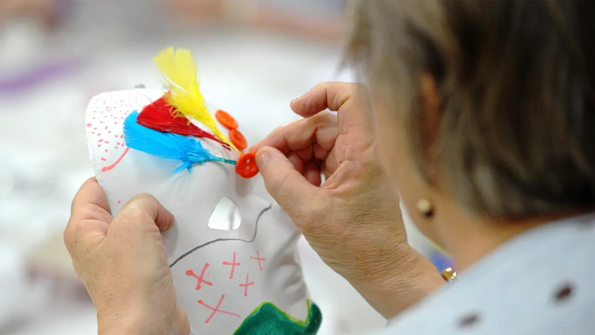 A lady sewing a button onto a mask during an arts and crafts session.