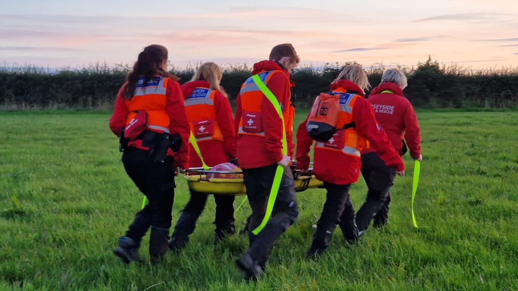 Merseyside Lowland Search and Rescue members carrying a stretcher across a field.