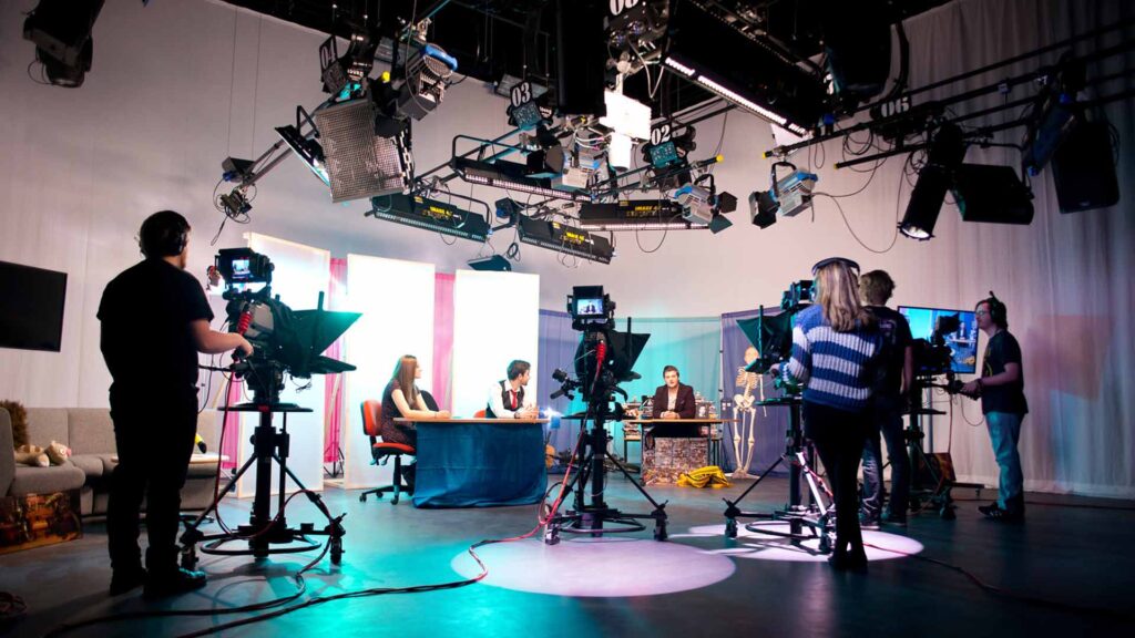 Edge Hill film students stood positioning cameras at two students sat at news desk.