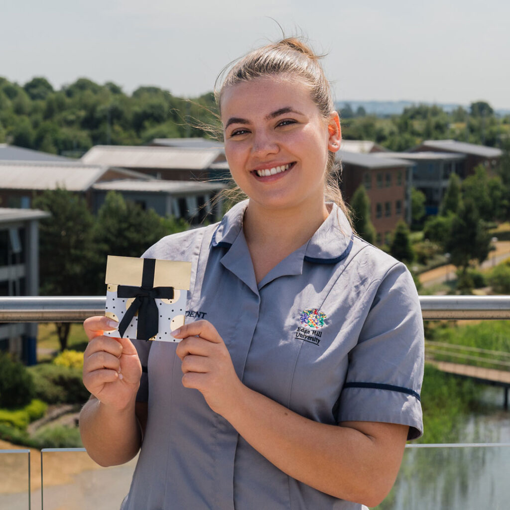 Image of medicine student Lauren stood on rooftop garden in Catalyst. She's holding the prize she won, a £25 Amazon voucher