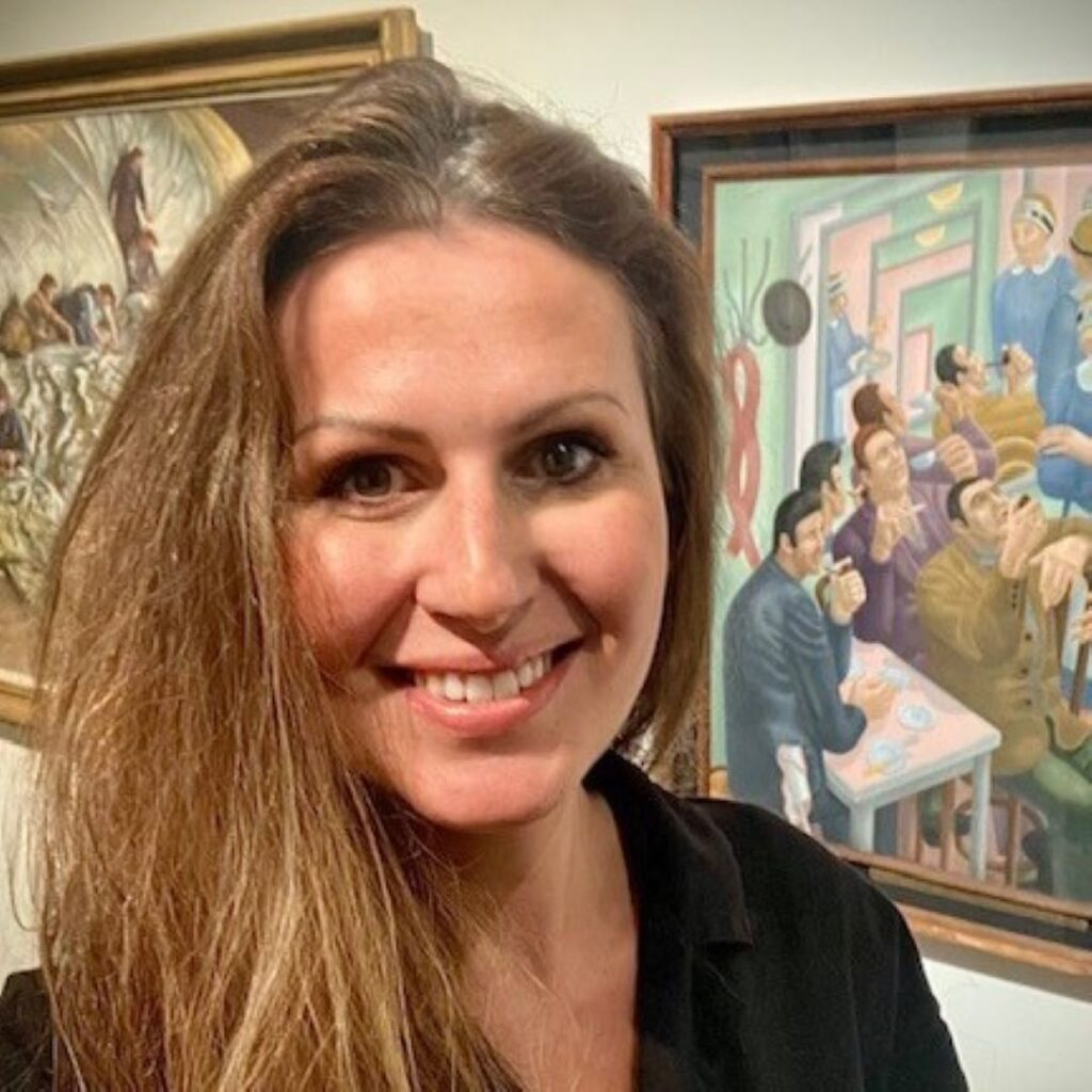 A picture of Gemma Grady Hill standing in front of two framed pictures.