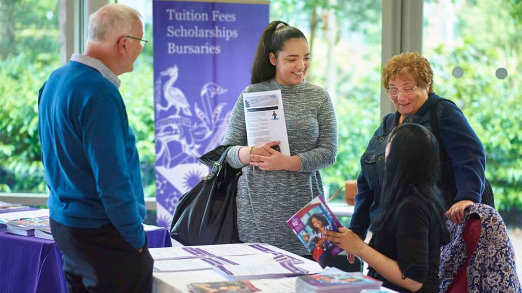 Image of visitor talking to staff member with banner saying 'Tuition Fees, Scholarships, Bursaries'