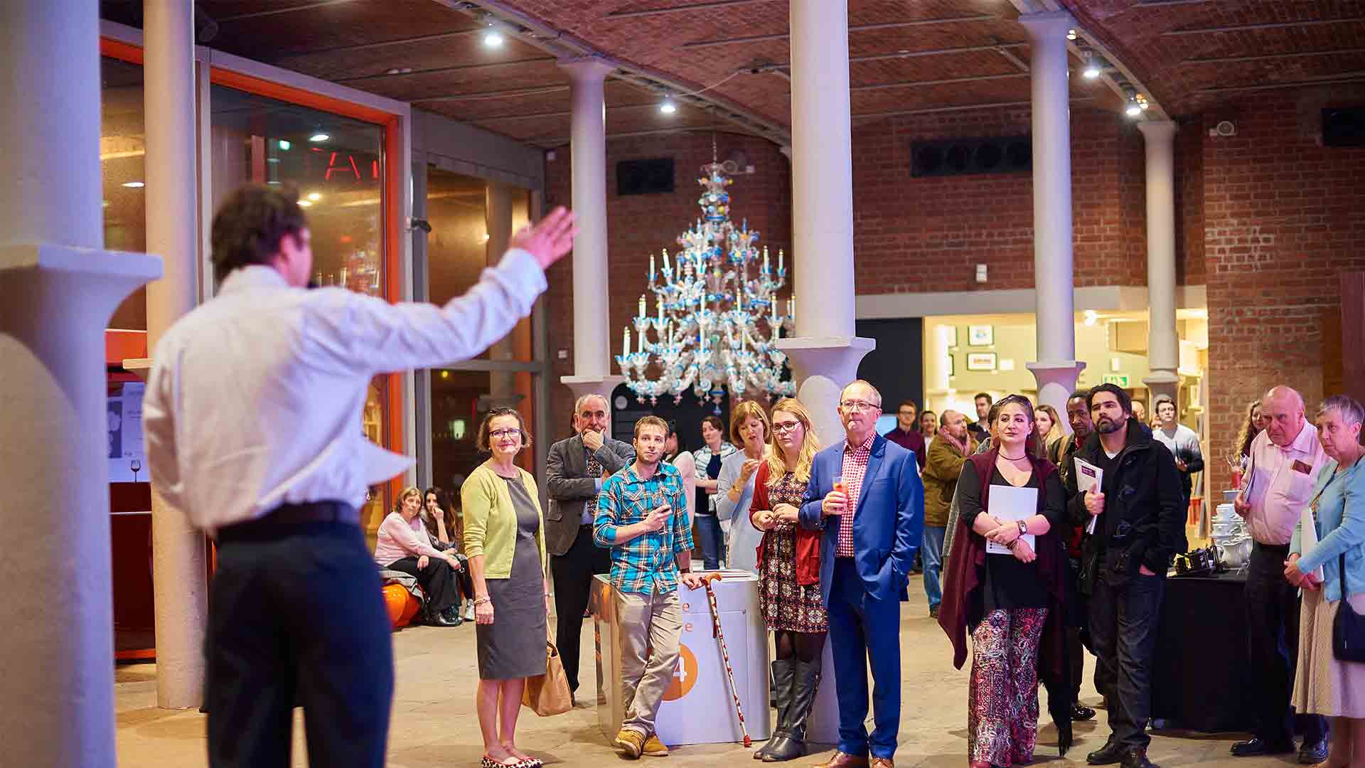 Guest speaker stood in a white dress shirt and trousers talking to a crowd.