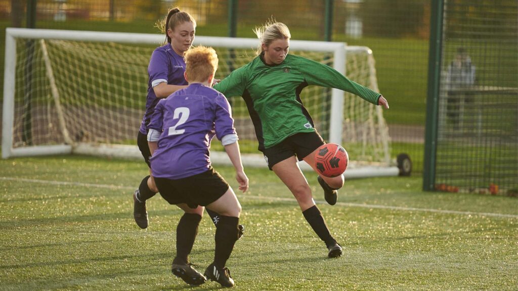 Image of of a football match taking place with a representative from the Women's Edge Hill football team playing against opponents