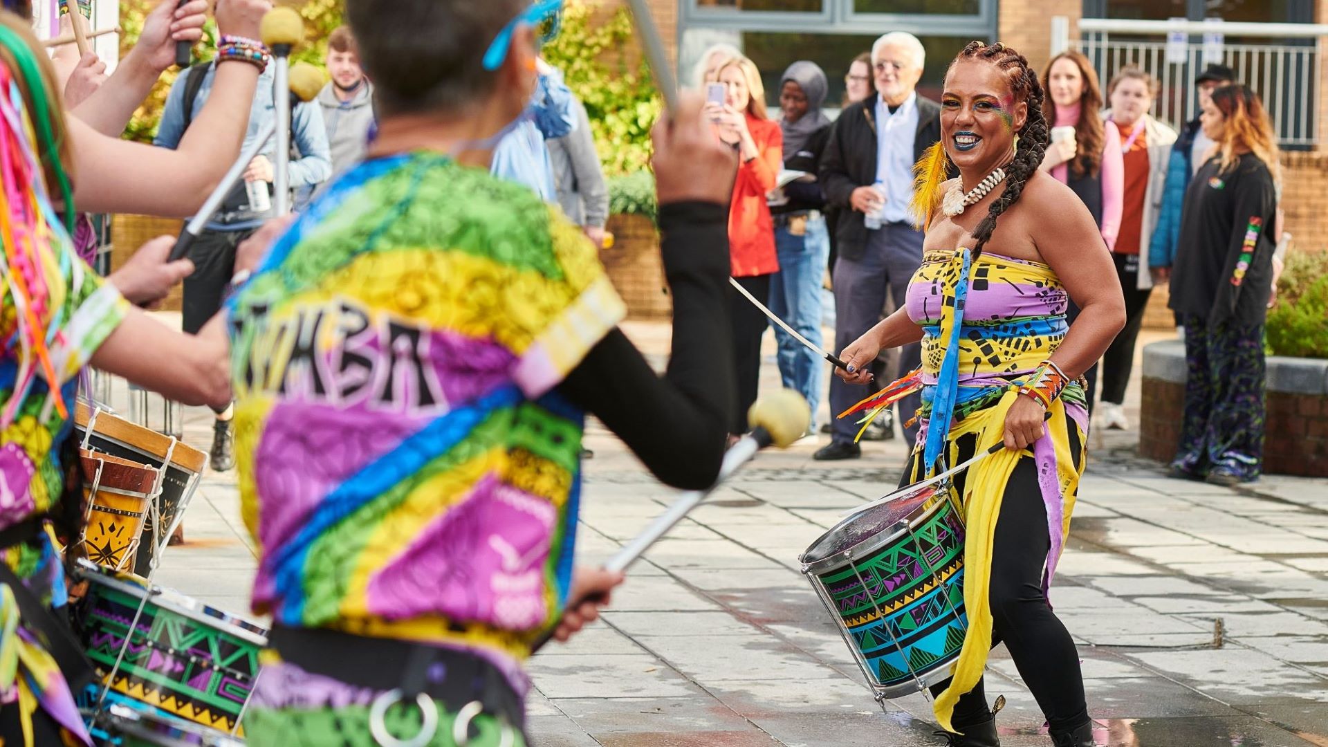 Colourfully-dressed drummers dance and beat their drums.