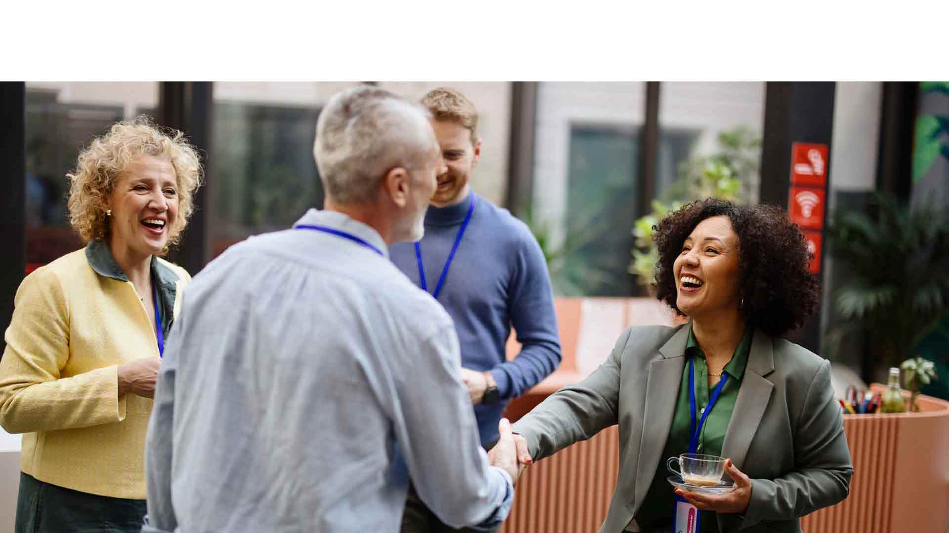 A group of people. A man and a woman are smiling at each other and shaking hands.