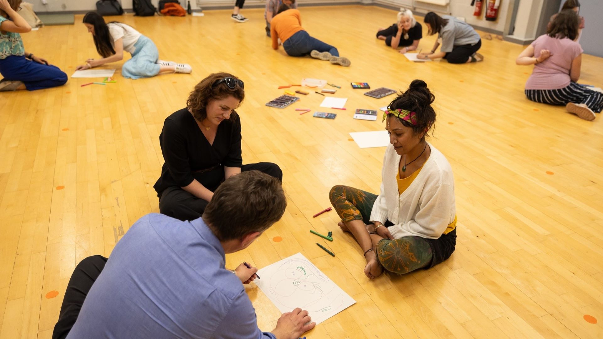 A group of people sitting on the floor using creative therapy. They are drawing.