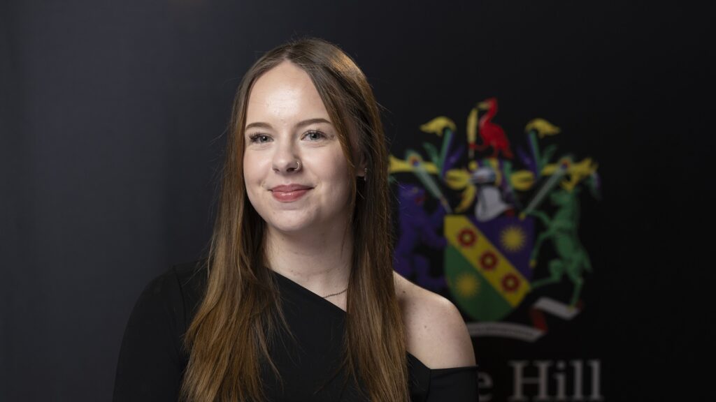 Jessica Riley smiles at the camera with an Edge Hill University emblem in the background