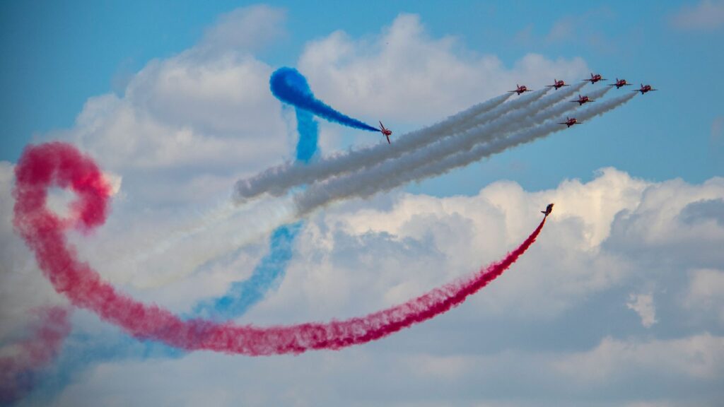 Red arrows aeroplanes doing some tricks with blue, white and red smoke in the sky.