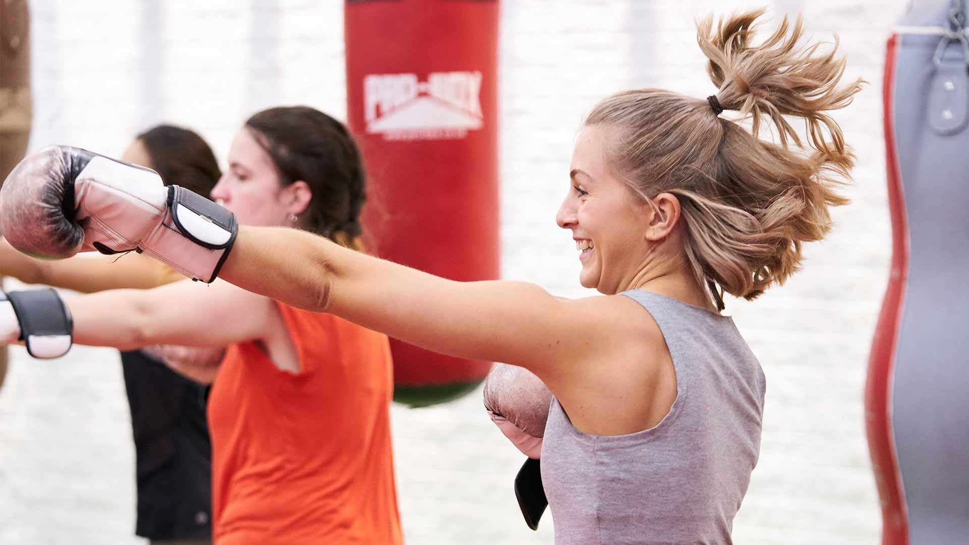 A blond woman wearing boxing gloves and punching a punch bag.