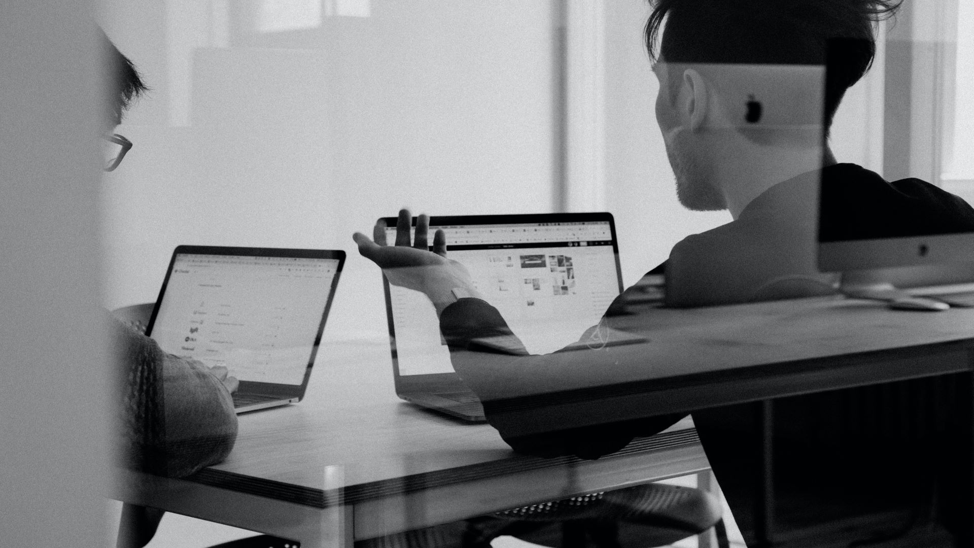 Two people in an office using laptops. The photo is black and white.