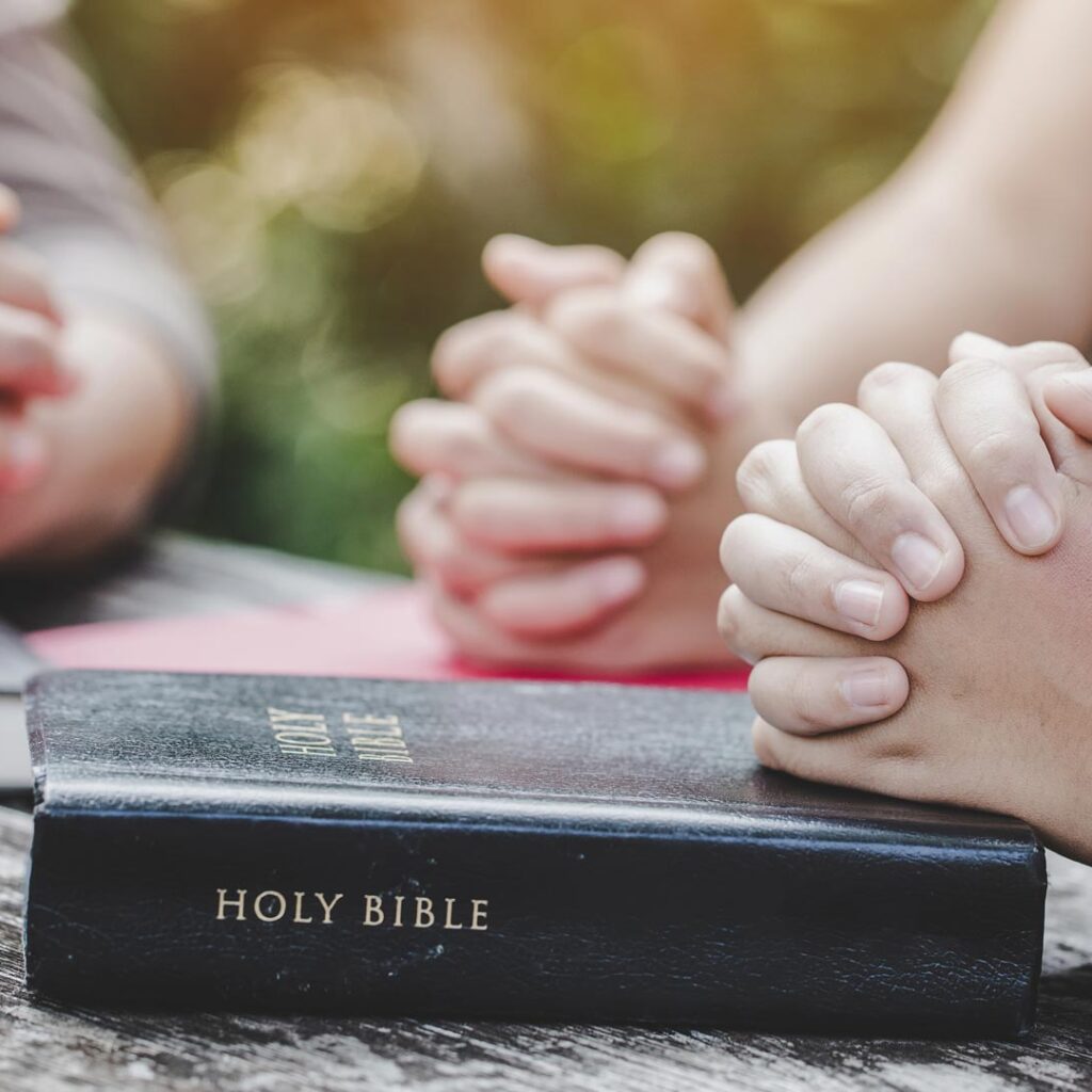 clasped hands in prayer on top of a bible