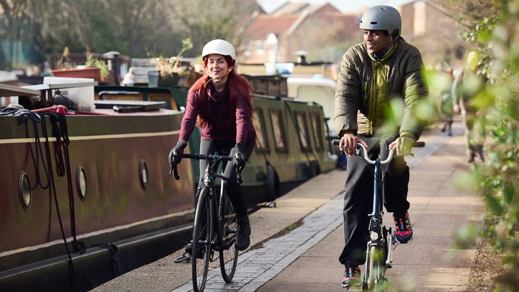Two people cycle alongside a river