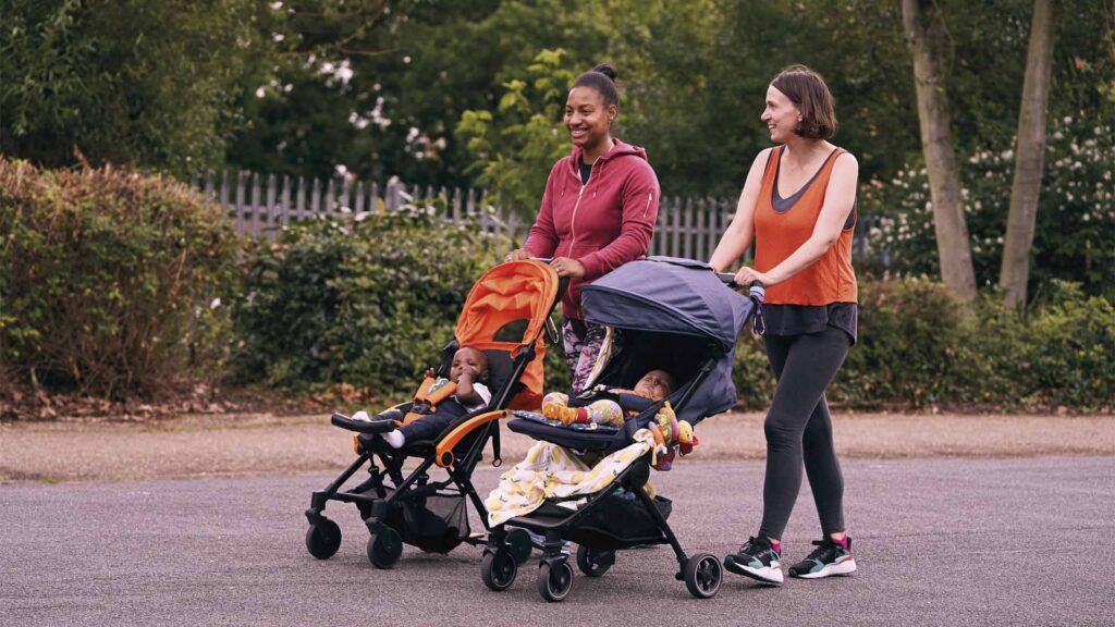 Two parents in gym wear pushing their children in prams