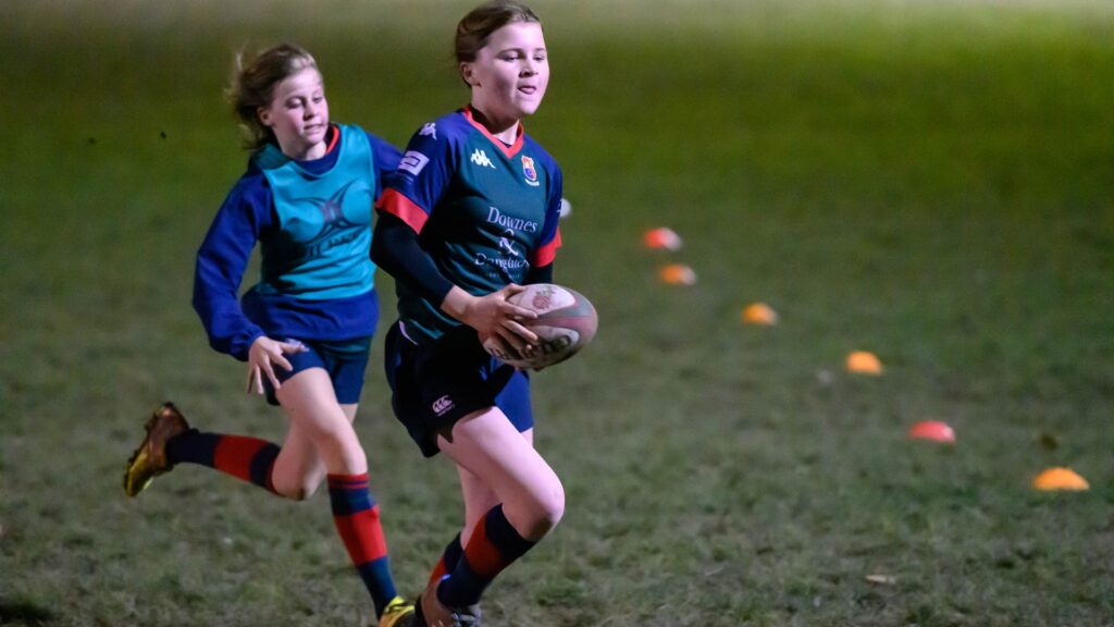 Two children playing rugby on a pitch