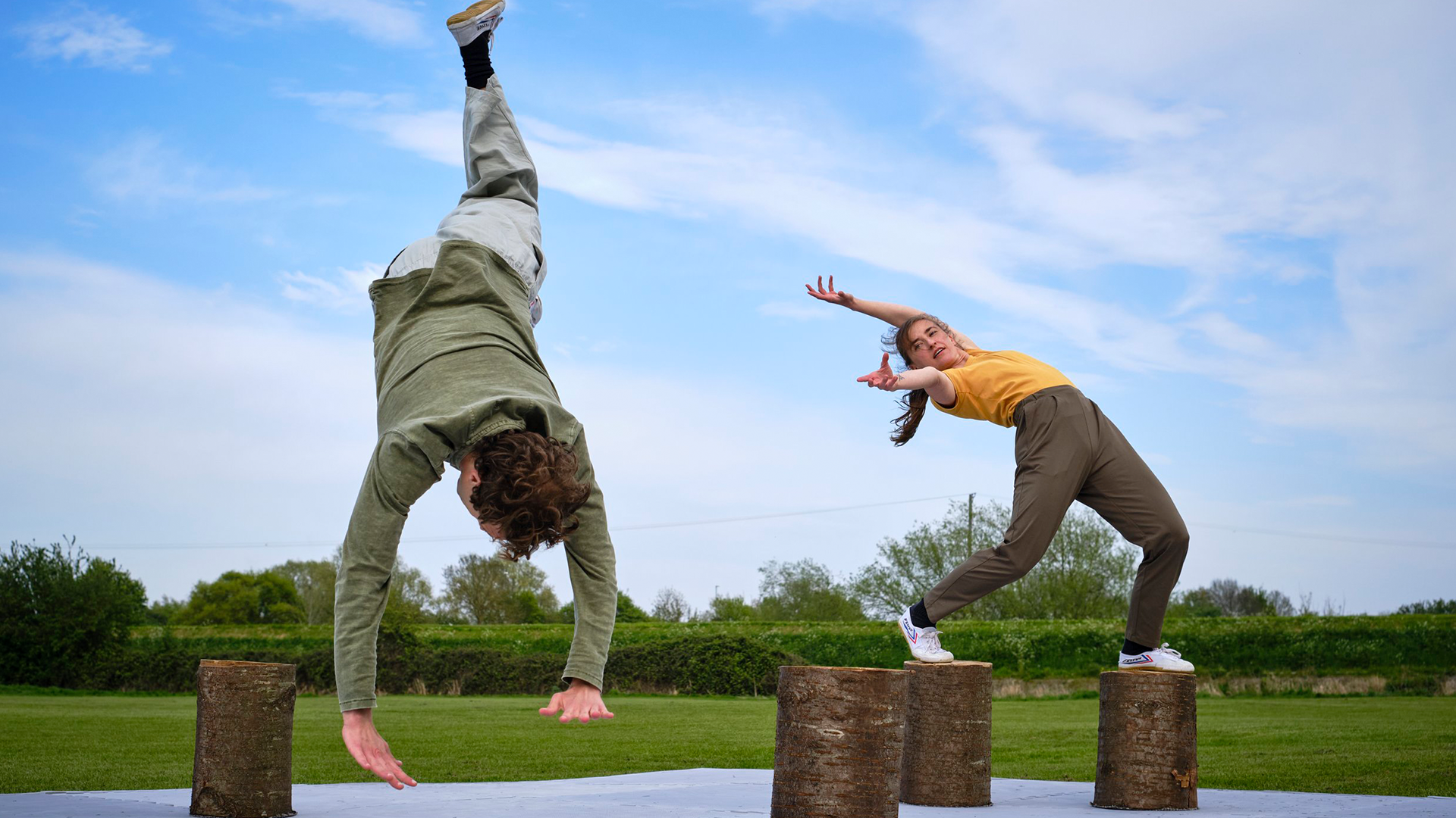 An image of dance students balancing on wooden stumps.