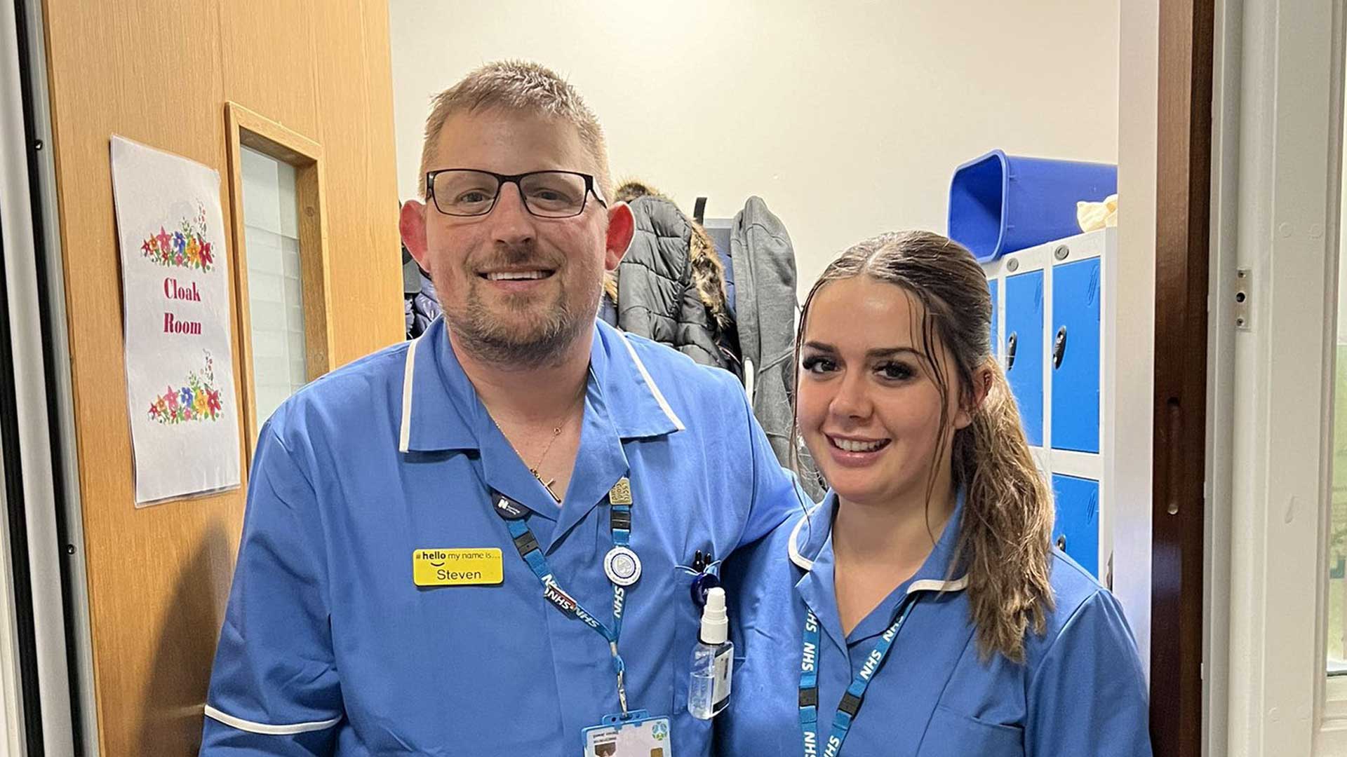 Steven and Stevie-Leigh stand close together wearing their nurses uniform and smile at the camera.
