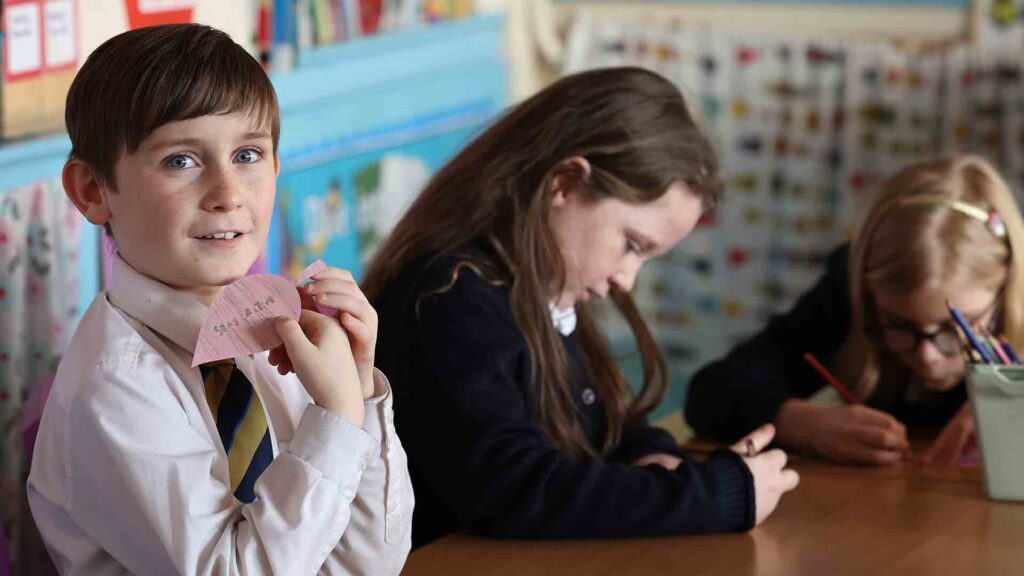 Primary aged school pupils sat at a desk in a classroom setting
