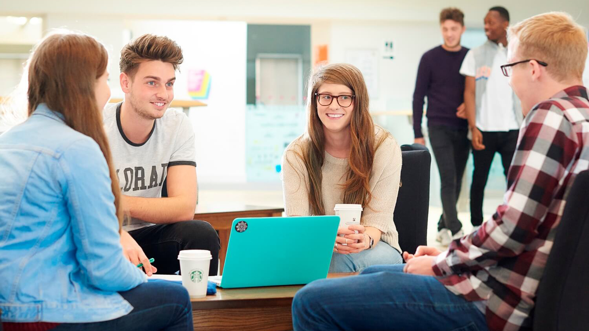 Four students chatting while sat round a table near the Students' Union offices in the Hub.