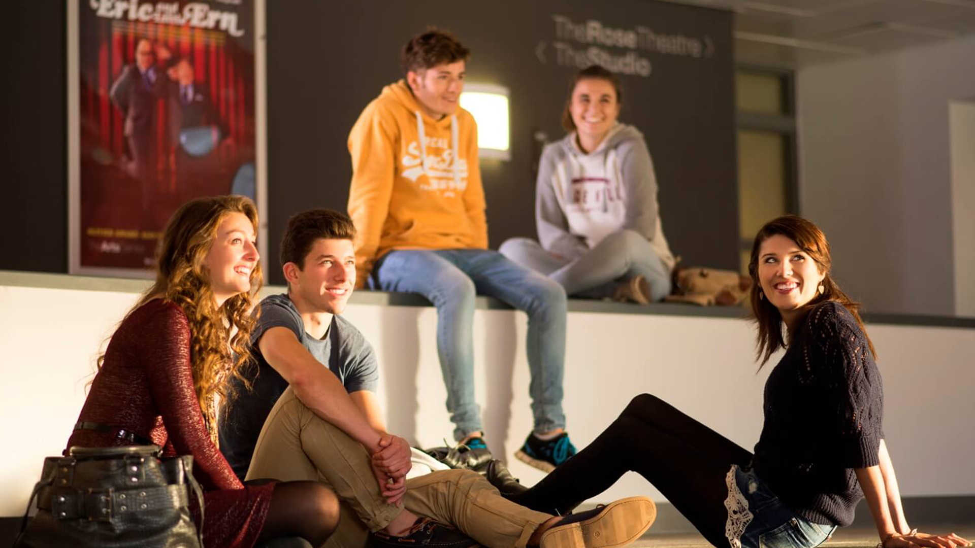 Three students sit on the floor in the Arts Centre while another two sit behind them on a low wall.