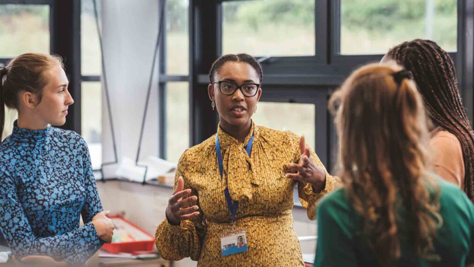 A shot of a mid-adult secondary school teacher talking with her sixth form students in class, they are wearing casual clothing and discussing what they learned in class, in a school in Gateshead, England.