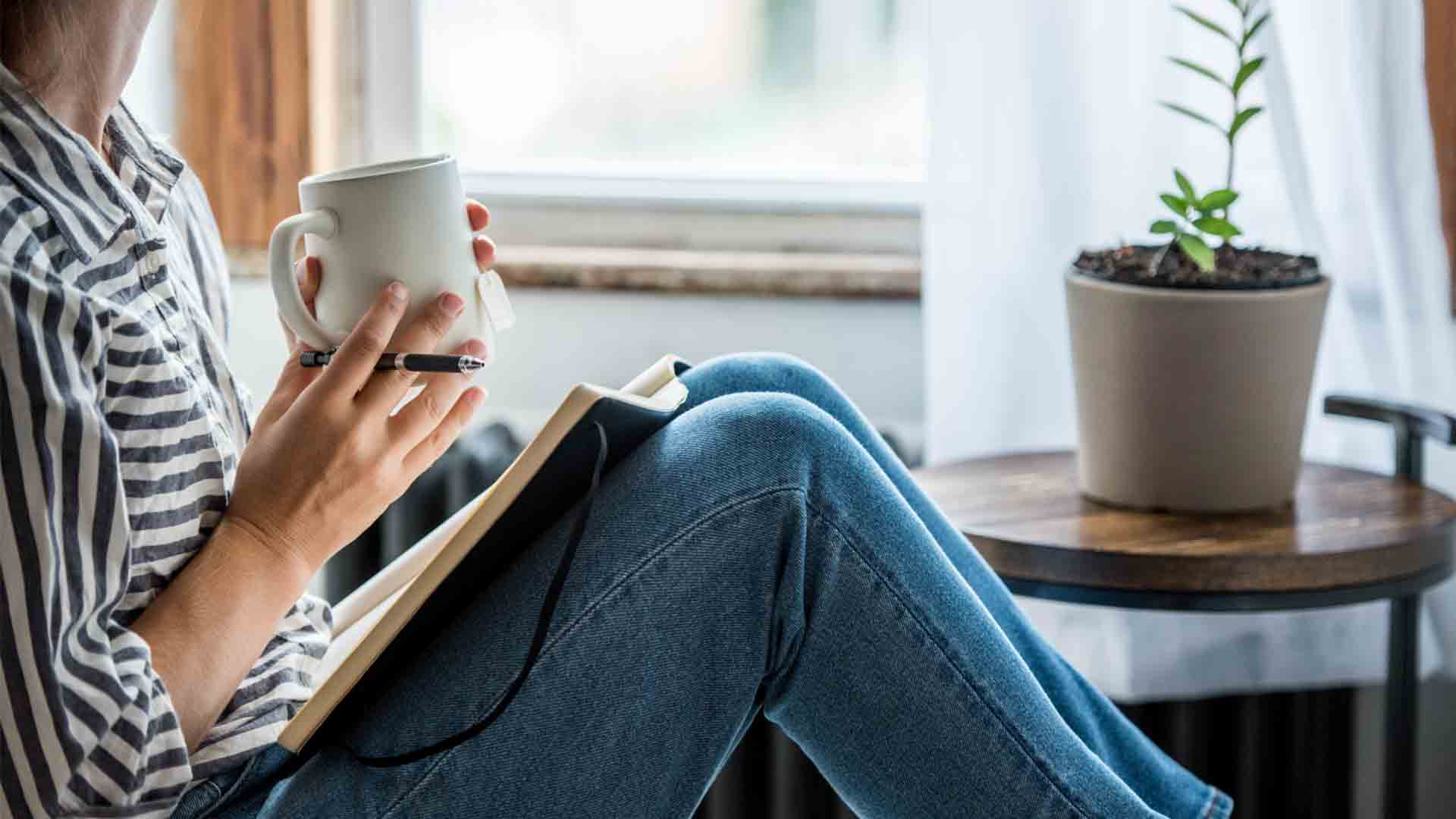 Adult sitting with mug, pen and open notebook