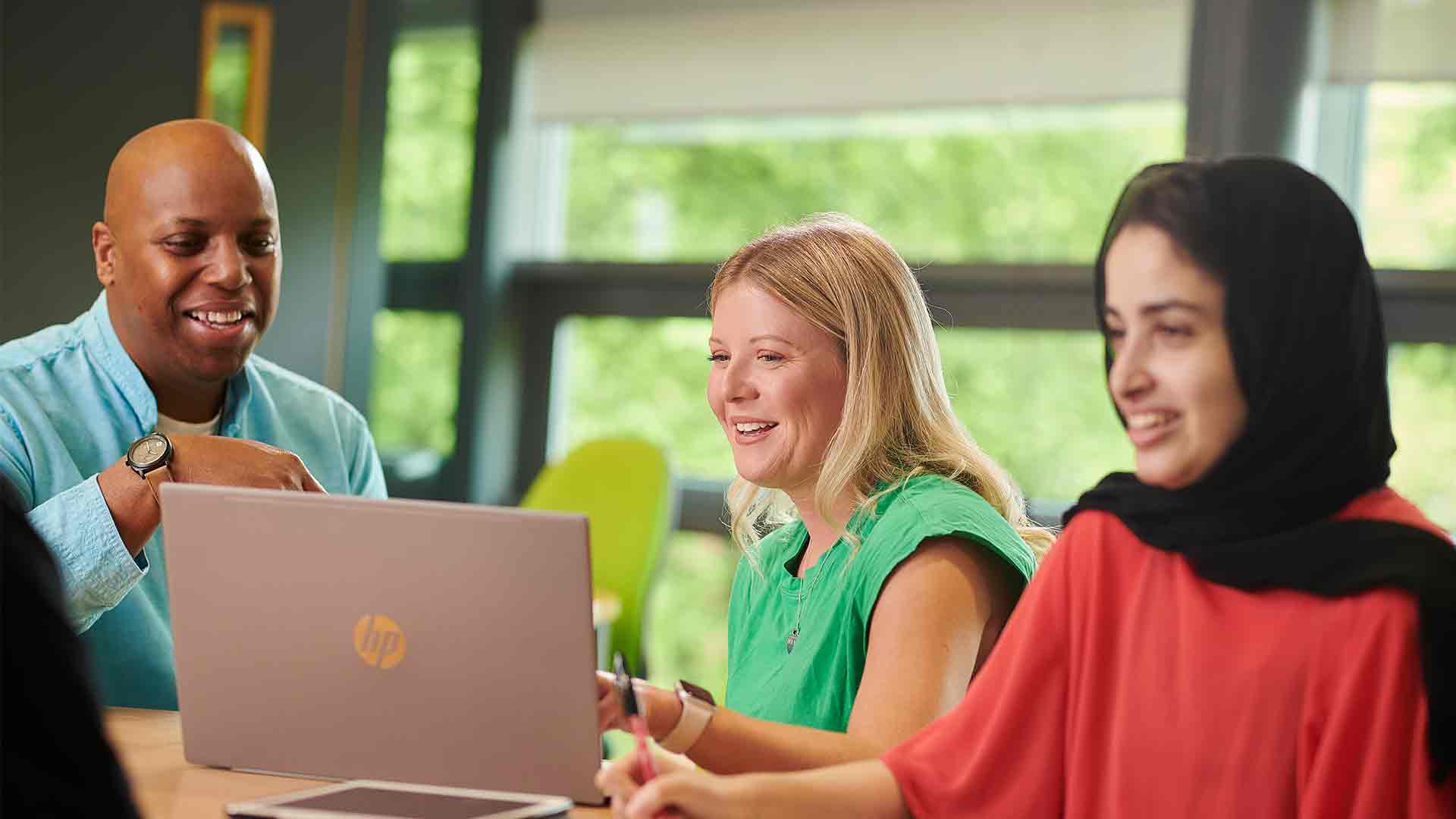 Three mature students sat around a desk looking at something on a laptop.