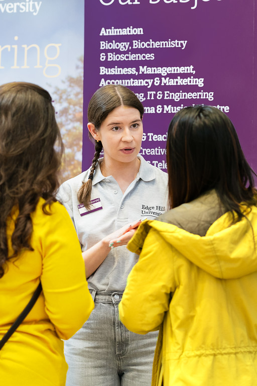 An Edge Hill staff member talks to two students at a HE Fair.