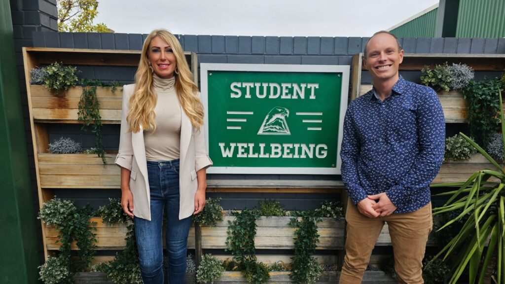 Nina Smith and Dr Sam McKay stand either side of a sign saying 'student wellbeing'