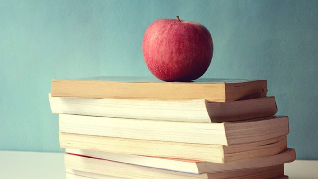 A red apple sits atop a pile of books.