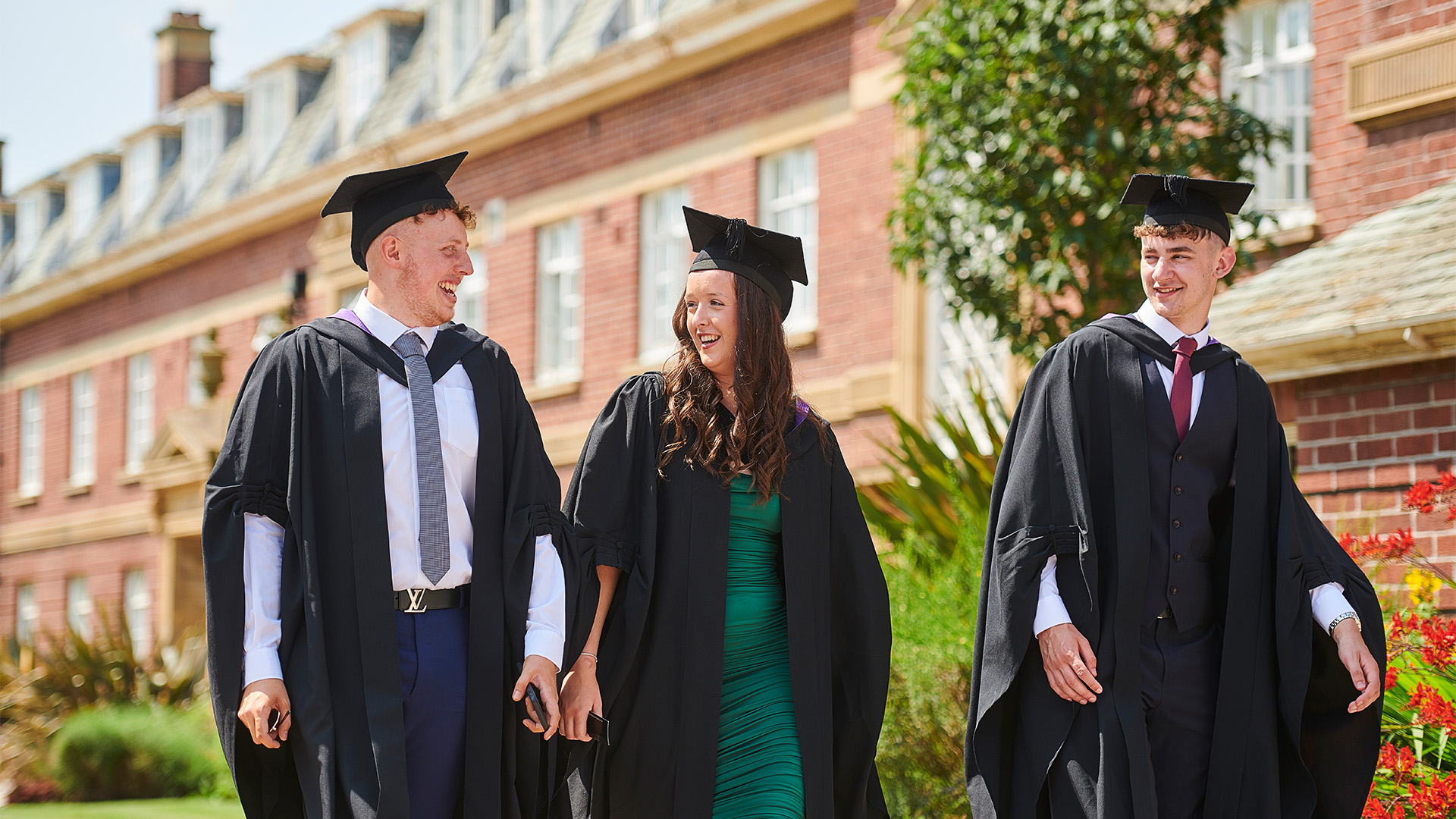 male and female graduate walking in cap and gown outside main building