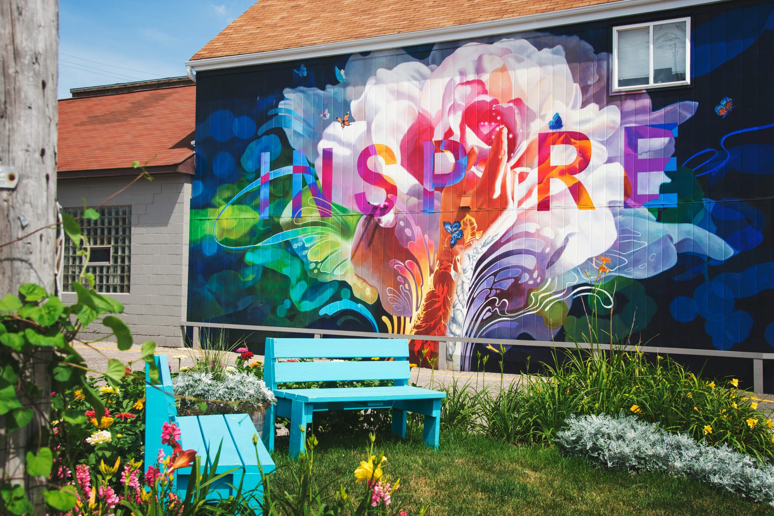A photo of a garden with bright blue benches and a colourful mural on a building with the word 'inspire'