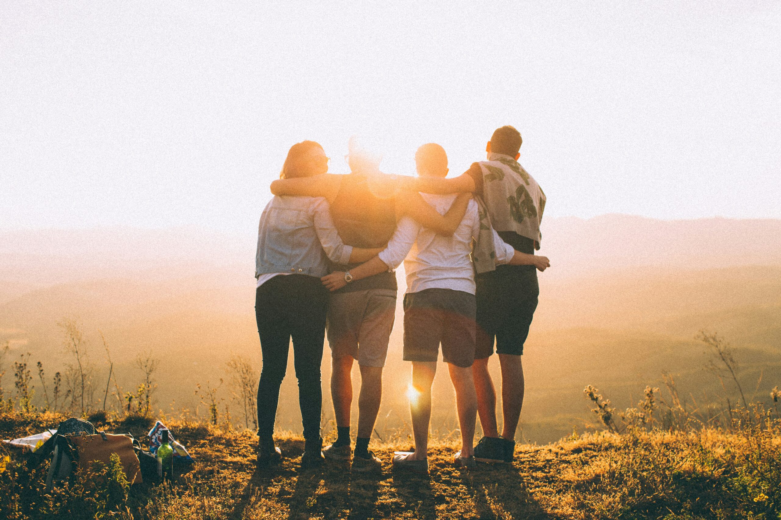A photo of four adults holding with their arms around each other in a line with a rural landscape on a sunny day - to represent a team