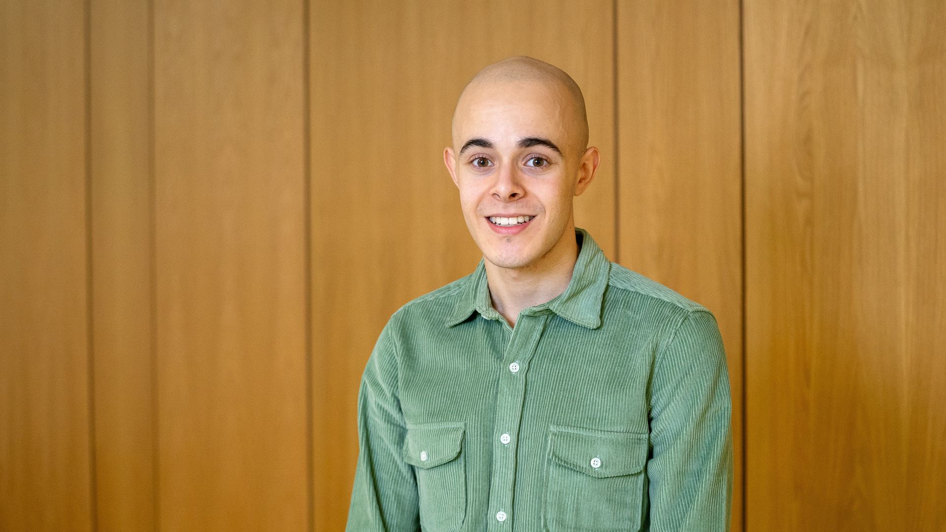 Michael Ellwood wears a green shirt and stands in front of a wood-panelled wall.