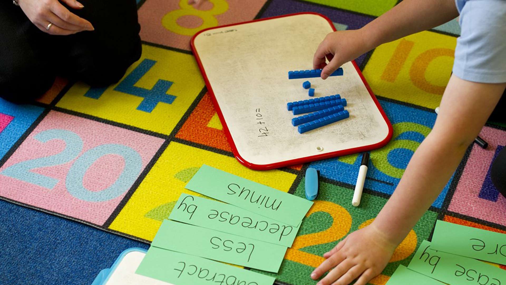 Child working with teacher using whiteboard and counting cubes in a maths activity.