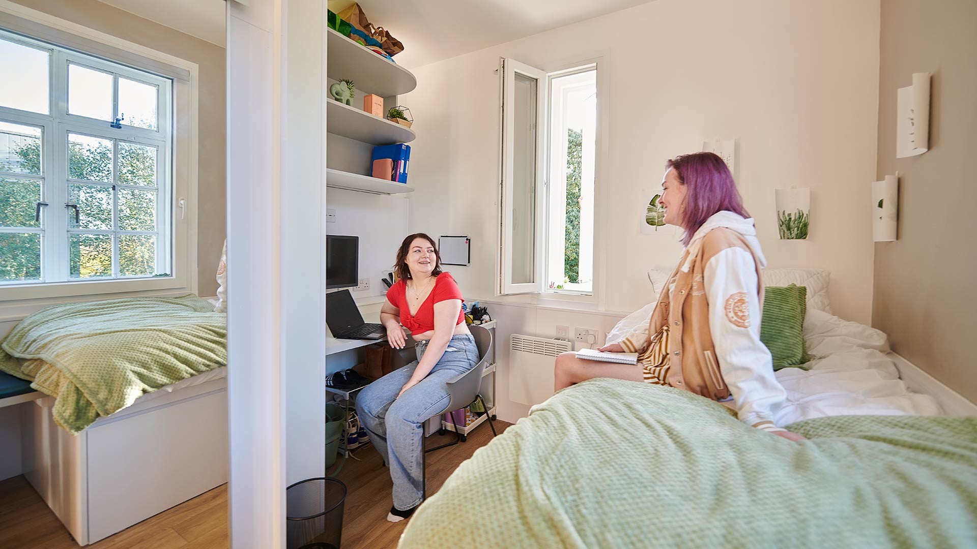 Two girls chatting in a room in halls on campus.