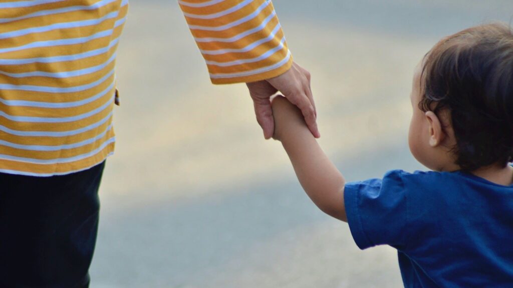 Young baby holding hands with mother while walking.
