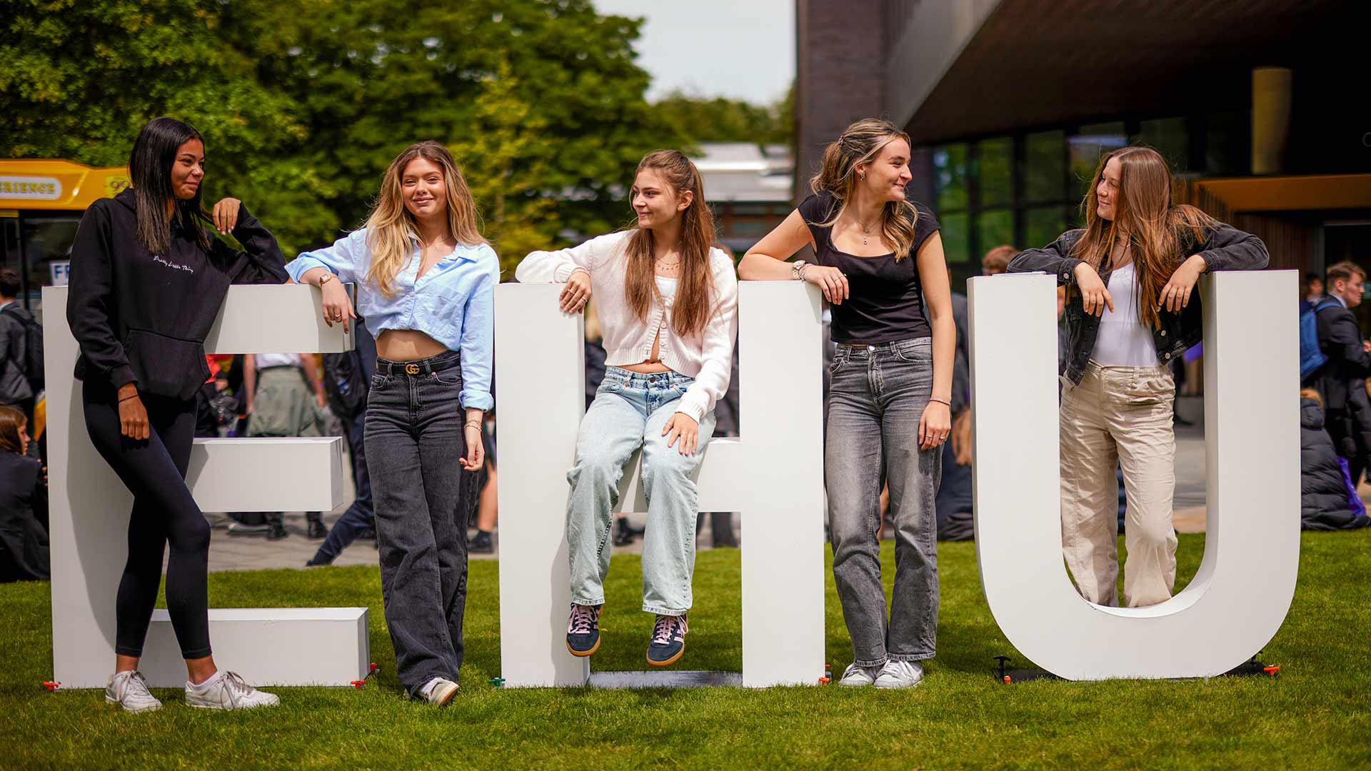 A group of college students exploring the campus on an open day, standing in front of the EHU letters