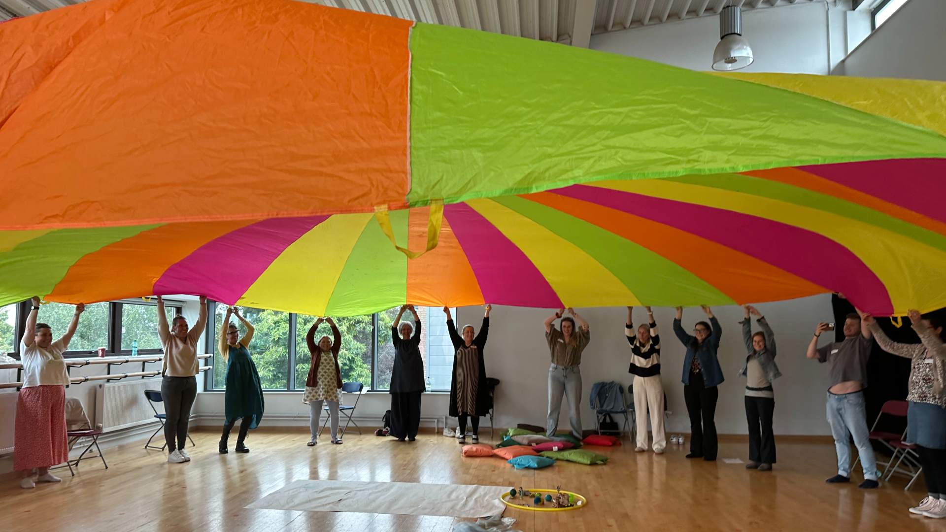 Group of people collectively in a circle under a multicoloured sheet of material