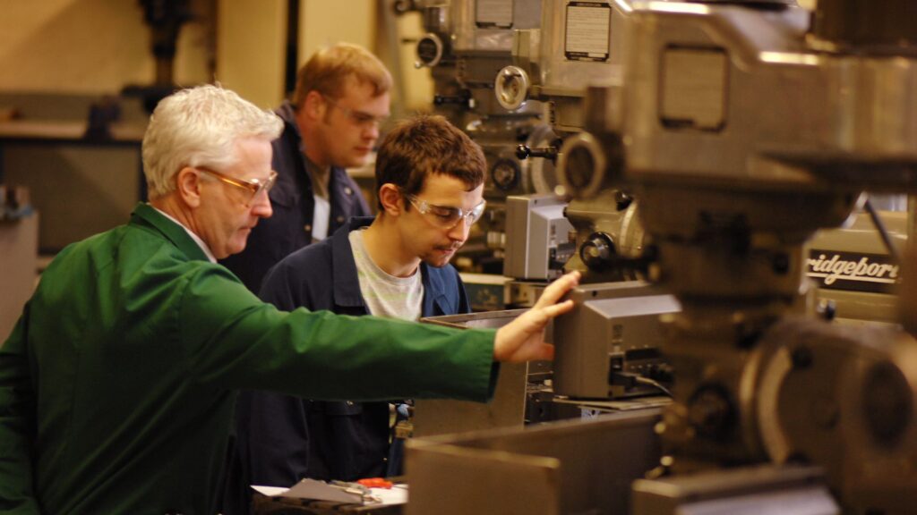A hands-on workshop scene showing a group of individuals working on industrial machinery