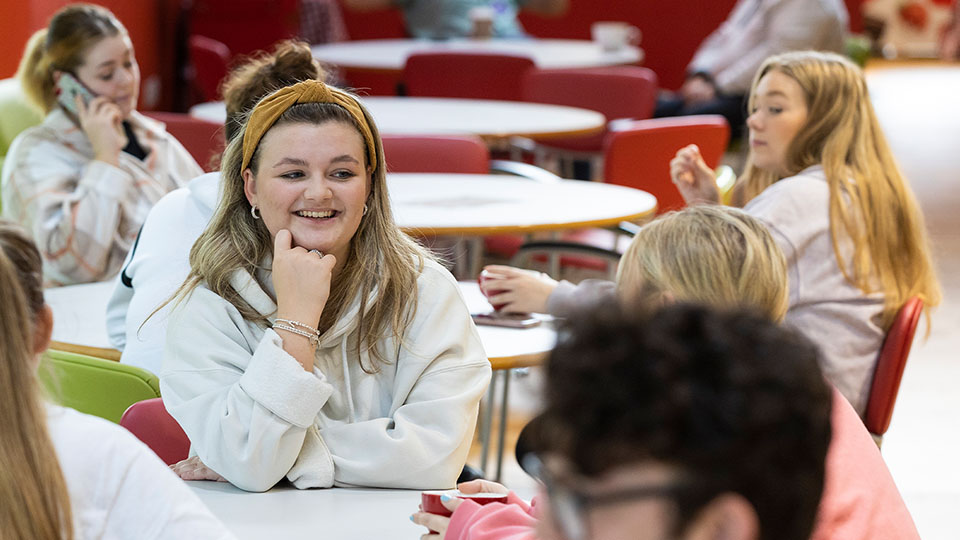 female student sat in the red bar smiling with friends