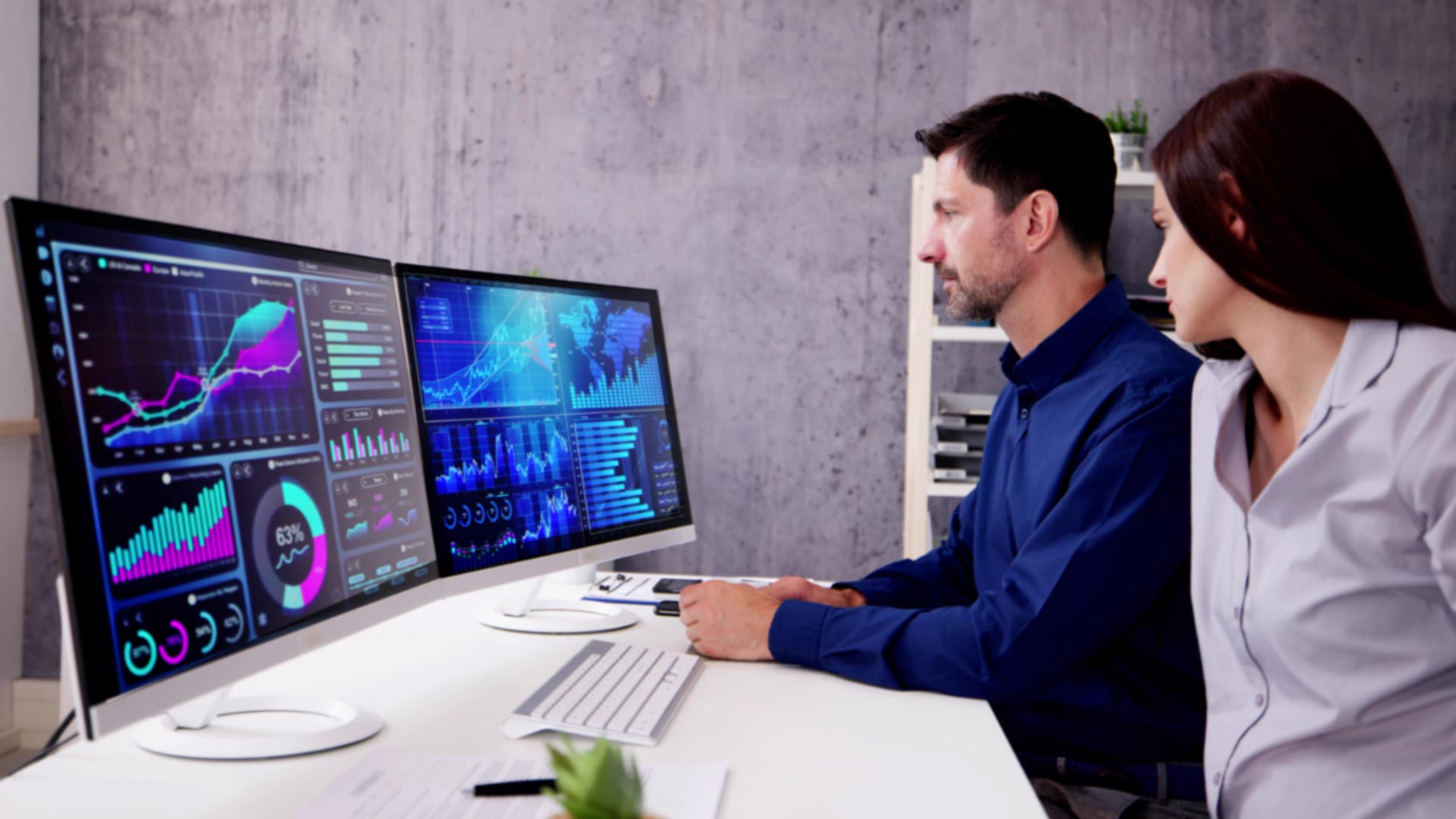 Two people at a computer looking at data and graphs on two monitors.